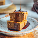 Deux parts carrées de gâteau à la patate douce sans gluten empilées sur une assiette, nappées d'un généreux filet de sirop d'érable