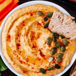 Houmous à la carotte sans gluten orangé dans un bol, filet d'huile d'olive et graines de sésame