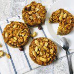 Trois tartelettes aux pommes vegan sans gluten parsemées de noix et d'amandes, avec une tartelette coupée sur une assiette blanche
