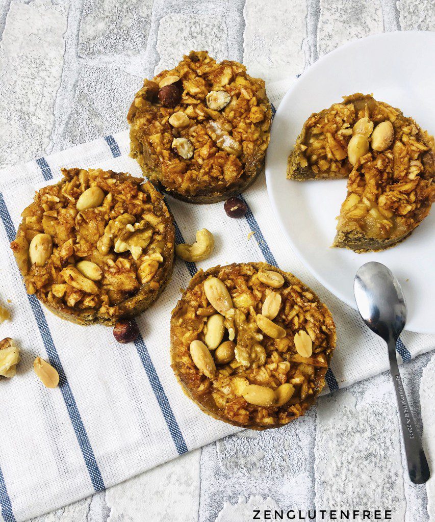 Trois tartelettes aux pommes vegan sans gluten parsemées de noix et d'amandes, avec une tartelette coupée sur une assiette blanche