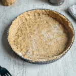 Fond de tarte en pâte sucrée sans gluten aux graines de chia piqué à la fourchette dans un moule noir.