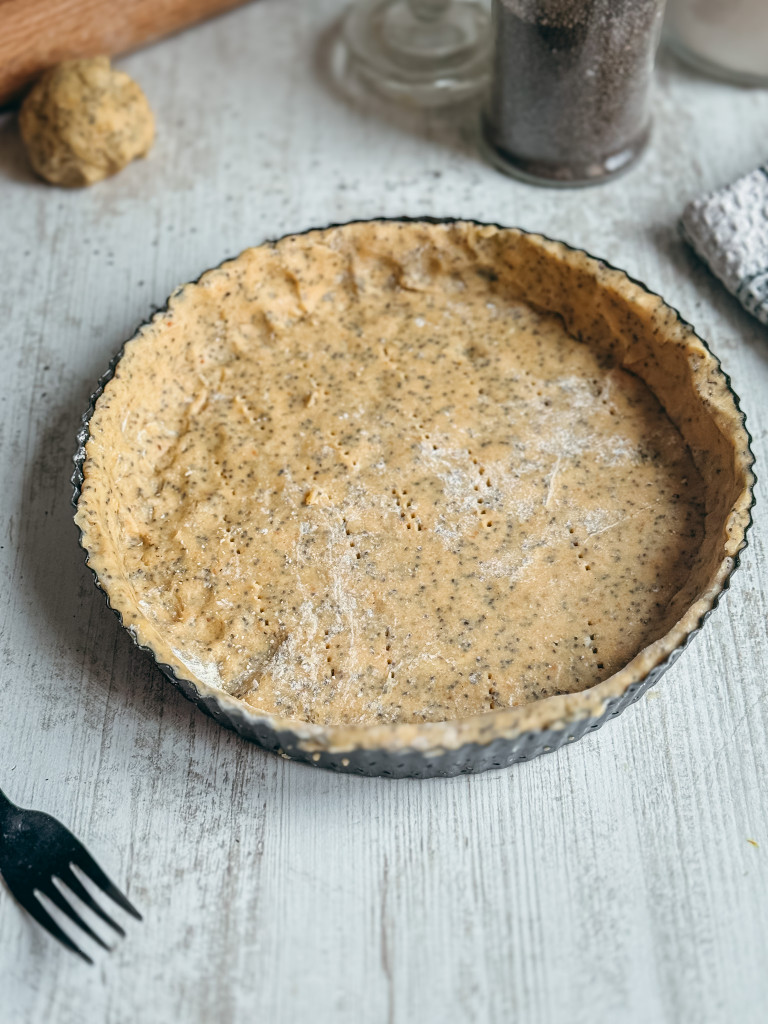 Fond de tarte en pâte sucrée sans gluten aux graines de chia piqué à la fourchette dans un moule noir.