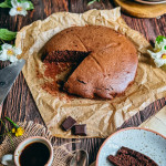 Moelleux au chocolat sans gluten rond avec une part coupée, posé sur du papier cuisson froissé sur une table en bois rustique.