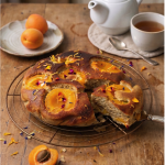 Gâteau moelleux à l'abricot sans gluten doré avec abricots caramélisés et fleurs comestibles sur grille de refroidissement