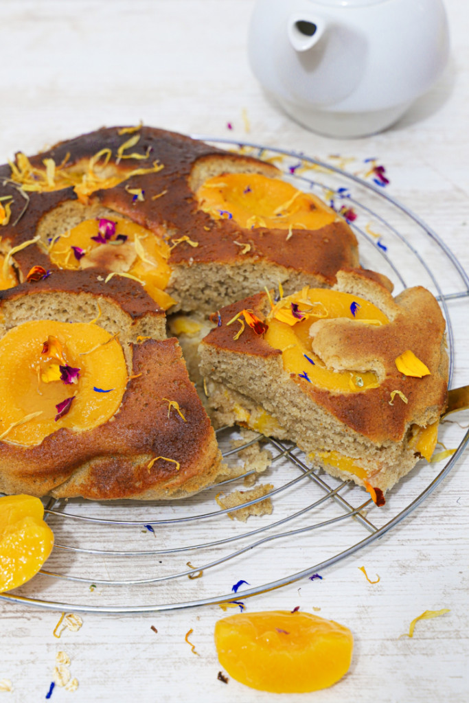 Gâteau moelleux à l'abricot sans gluten doré avec abricots caramélisés et fleurs comestibles sur grille de refroidissement