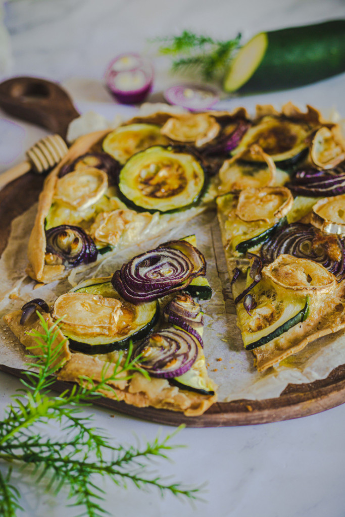 Tarte fine à la courgette sans gluten avec rondelles de courgette et oignon rouge sur pâte brisée dorée et croustillante
