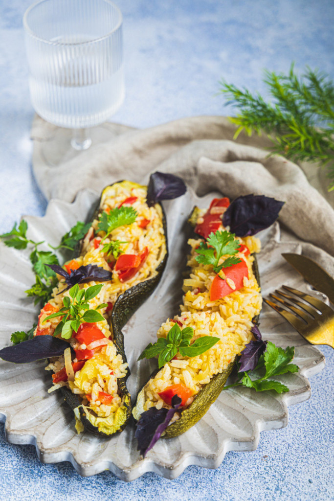 Courgettes farcies végétaliennes et sans gluten en bateaux avec farce de riz, poivron rouge et herbes fraîches sur assiette texturée