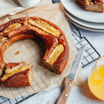 Banana bread sans gluten en forme de couronne avec des tranches de bananes caramélisées sur le dessus posé sur du papier cuisson