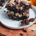 Brownie fondant au chocolat sans gluten découpé en carrés, parsemé de noisettes concassées, sur une planche en bois