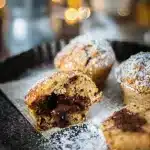 Muffins sans gluten saupoudrés de sucre glace, dont un est coupé en deux pour révéler un cœur coulant au chocolat fondant