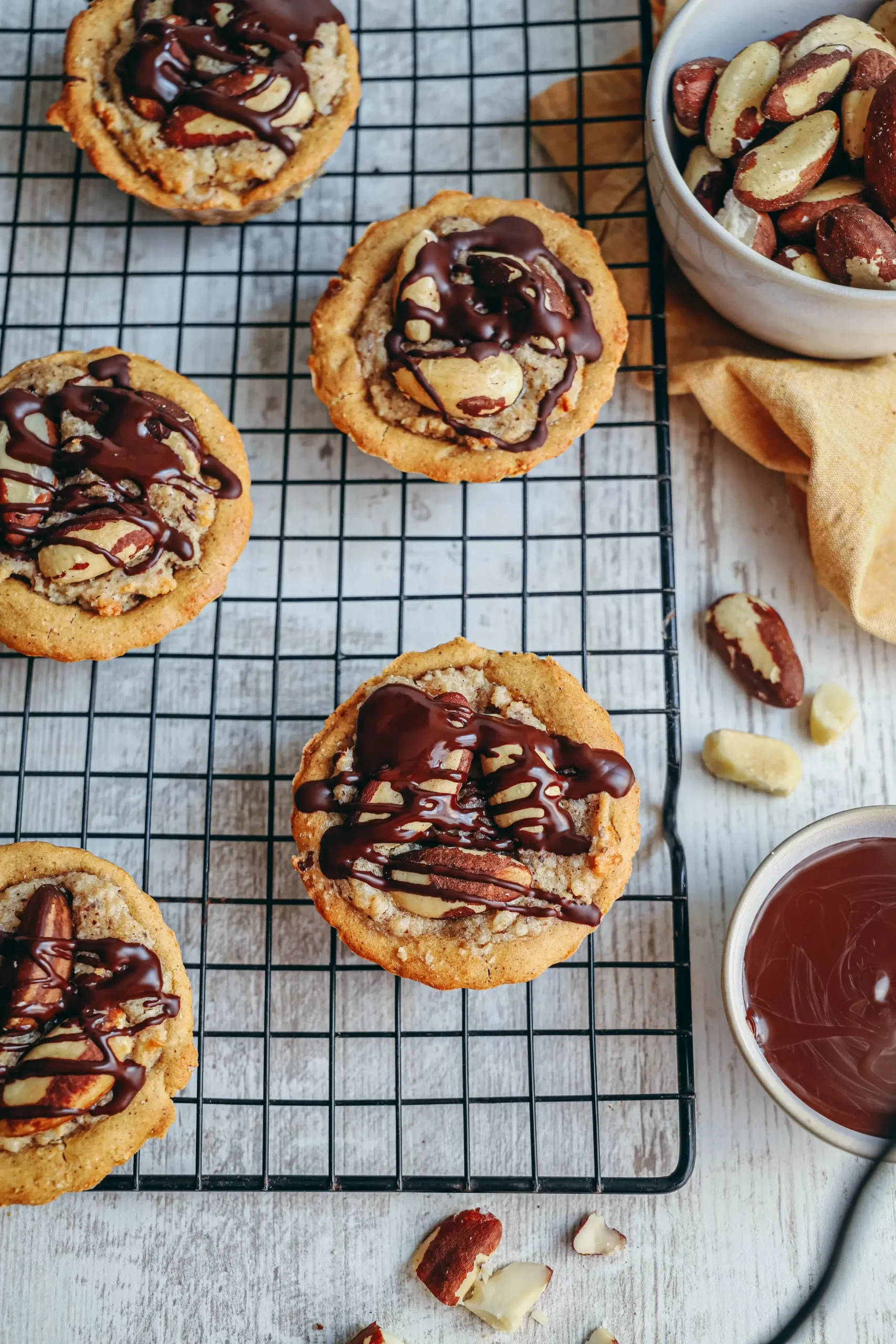Tartelettes aux noix du Brésil sans gluten croustillantes avec un nappage de chocolat noir fondu et des éclats de noix sur une grille