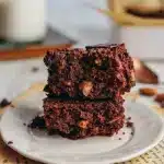 Trois carrés de brownie à la carotte sans gluten empilés sur une assiette blanche, texture fondante avec noix apparentes