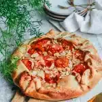Tarte rustique à l'abricot sans gluten aux bords repliés, garnie d'abricots rôtis et parsemée d'amandes effilées sur une planche en bois