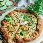 Tarte fine à la courgette sans gluten avec rondelles de courgette dorées pâte brisée croustillante et burrata crémeuse sur papier sulfurisé