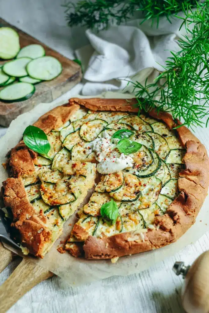 Tarte fine à la courgette sans gluten avec rondelles de courgette dorées pâte brisée croustillante et burrata crémeuse sur papier sulfurisé