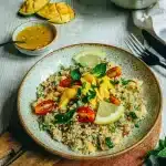 Taboulé de fonio sans gluten coloré garni de lamelles de mangue, tomates cerises, menthe et citron dans une assiette rustique