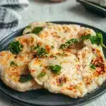 Naans moelleux sans gluten dorés et empilés dans une assiette noire avec persil frais et huile à l'ail