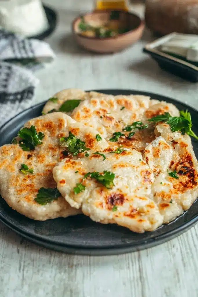 Naans moelleux sans gluten dorés et empilés dans une assiette noire avec persil frais et huile à l'ail