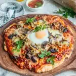 Pâte à pizza moelleuse sans gluten garnie de champignons olives oeuf et persil frais sur planche en bois