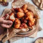 Beignets à la banane sans gluten sans lactose dorés et croustillants dans un bol en papier kraft avec main qui en prend un