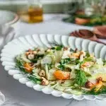 Salade de fenouil sans gluten avec clémentines avocat noix torréfiées et copeaux de parmesan sur assiette blanche