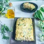 Quiche aux blettes et au chèvre sans gluten dorée et crémeuse sur plateau noir avec romarin frais et fleurs blanches