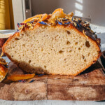 Gâteau au millet sans gluten bien doré et moelleux coupé en deux avec mie aérienne parsemé de fleurs séchées sur planche en bois
