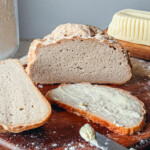 Pain sans gluten croustillant et moelleux fendu sur le dessus avec une tranche beurrée et un couteau sur une planche en bois rustique