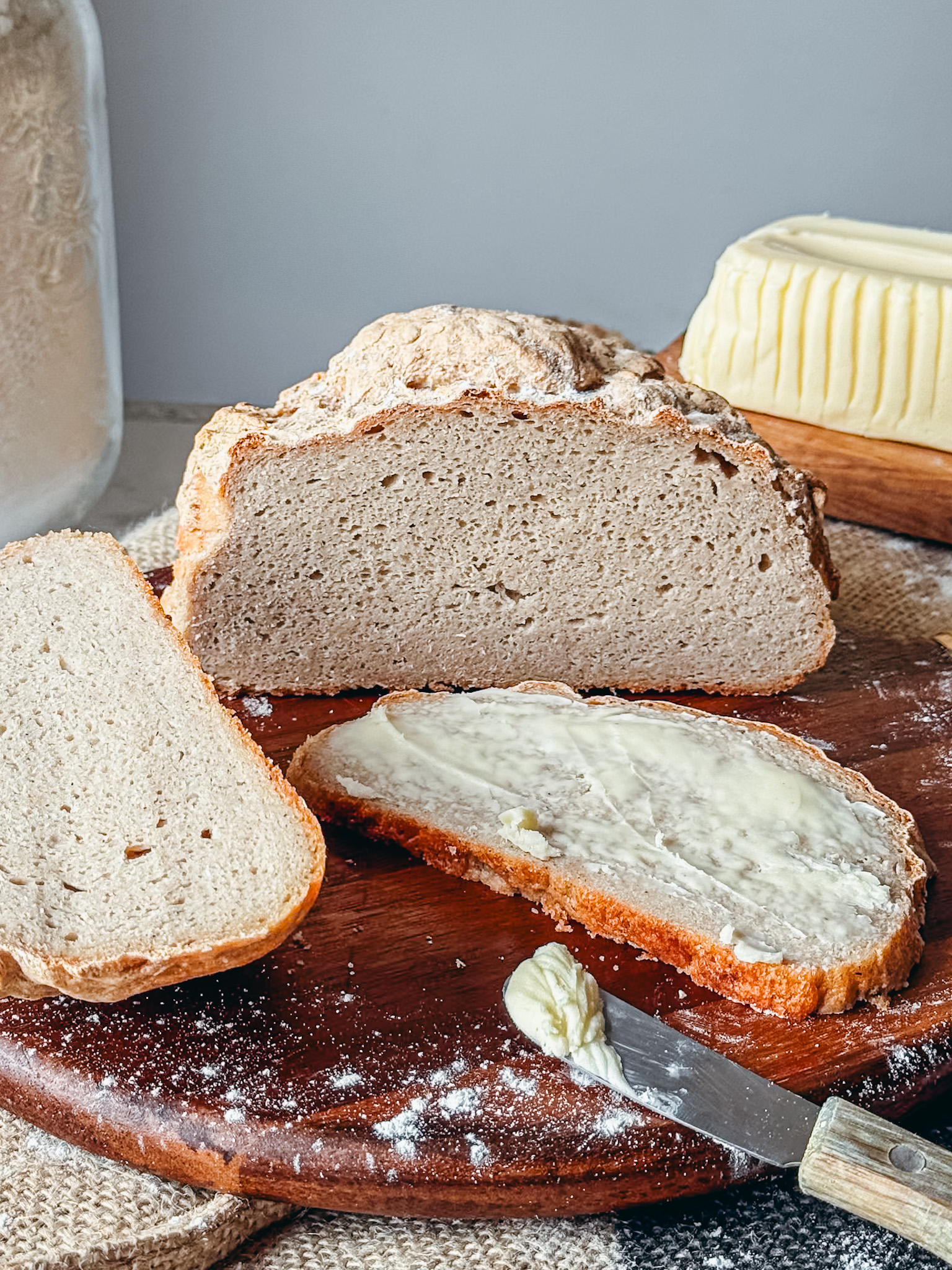Pain sans gluten croustillant et moelleux fendu sur le dessus avec une tranche beurrée et un couteau sur une planche en bois rustique